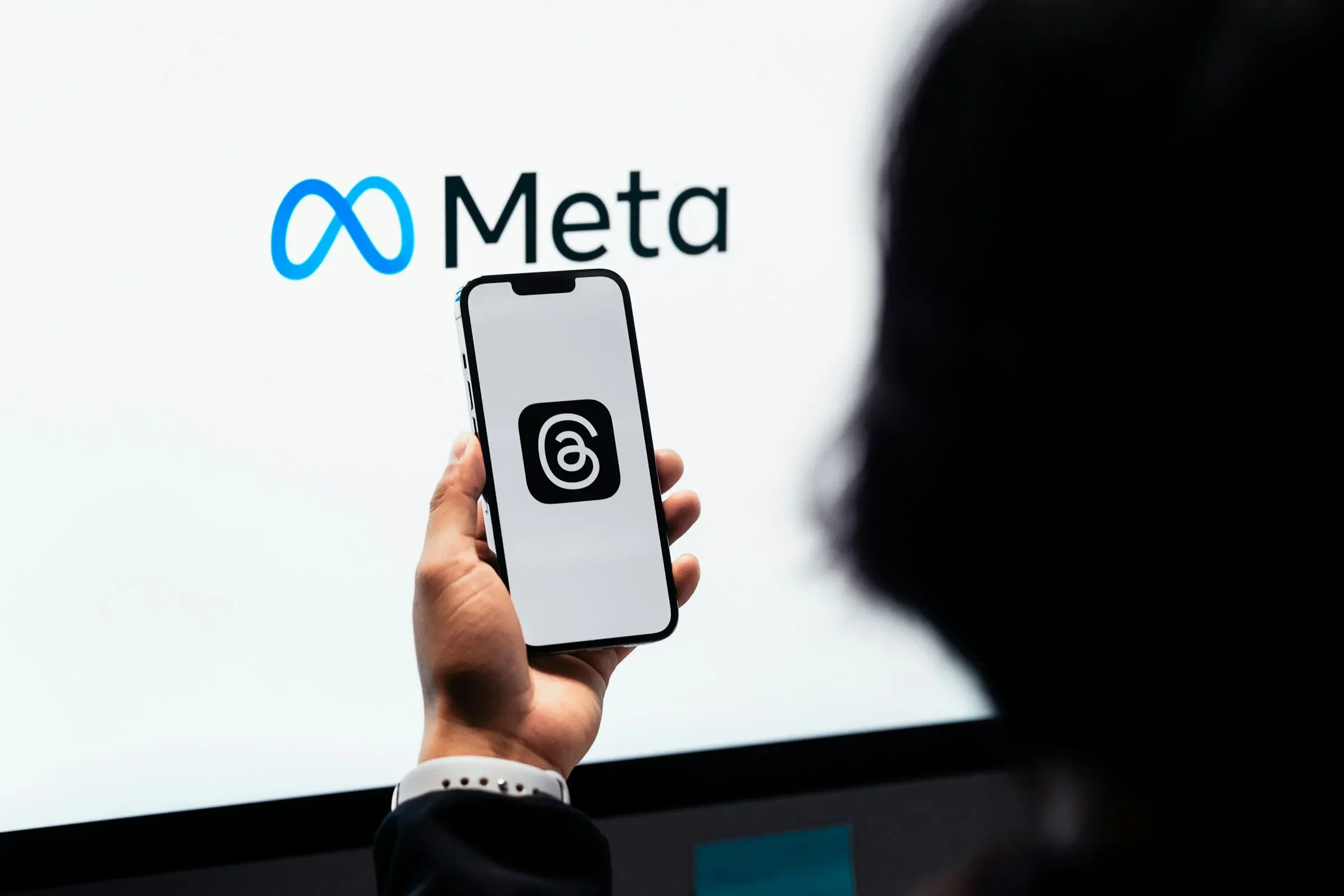 A hand holding a phone in front of a large Meta logo.