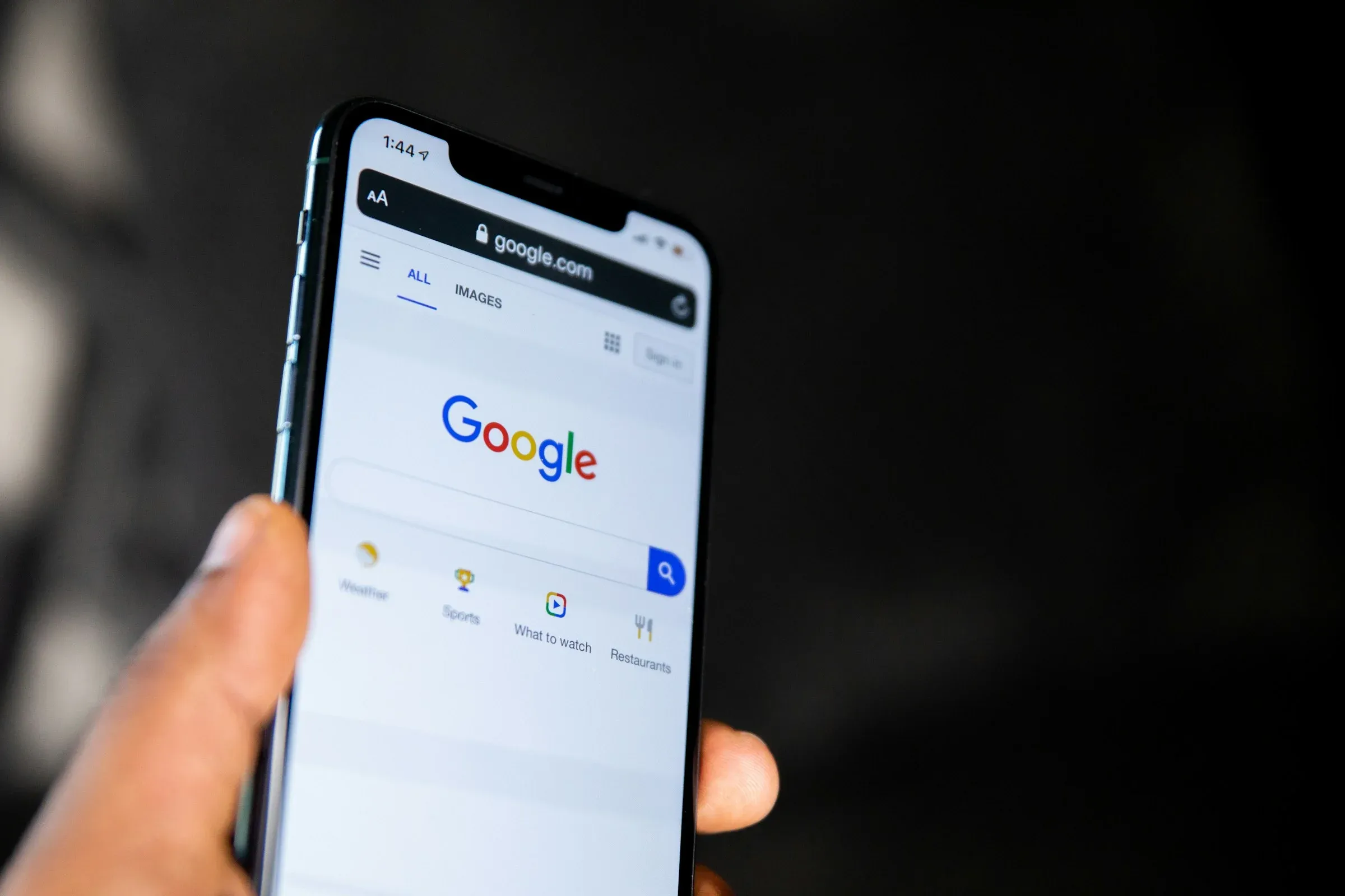 A hand holding a phone open on the Google search page.